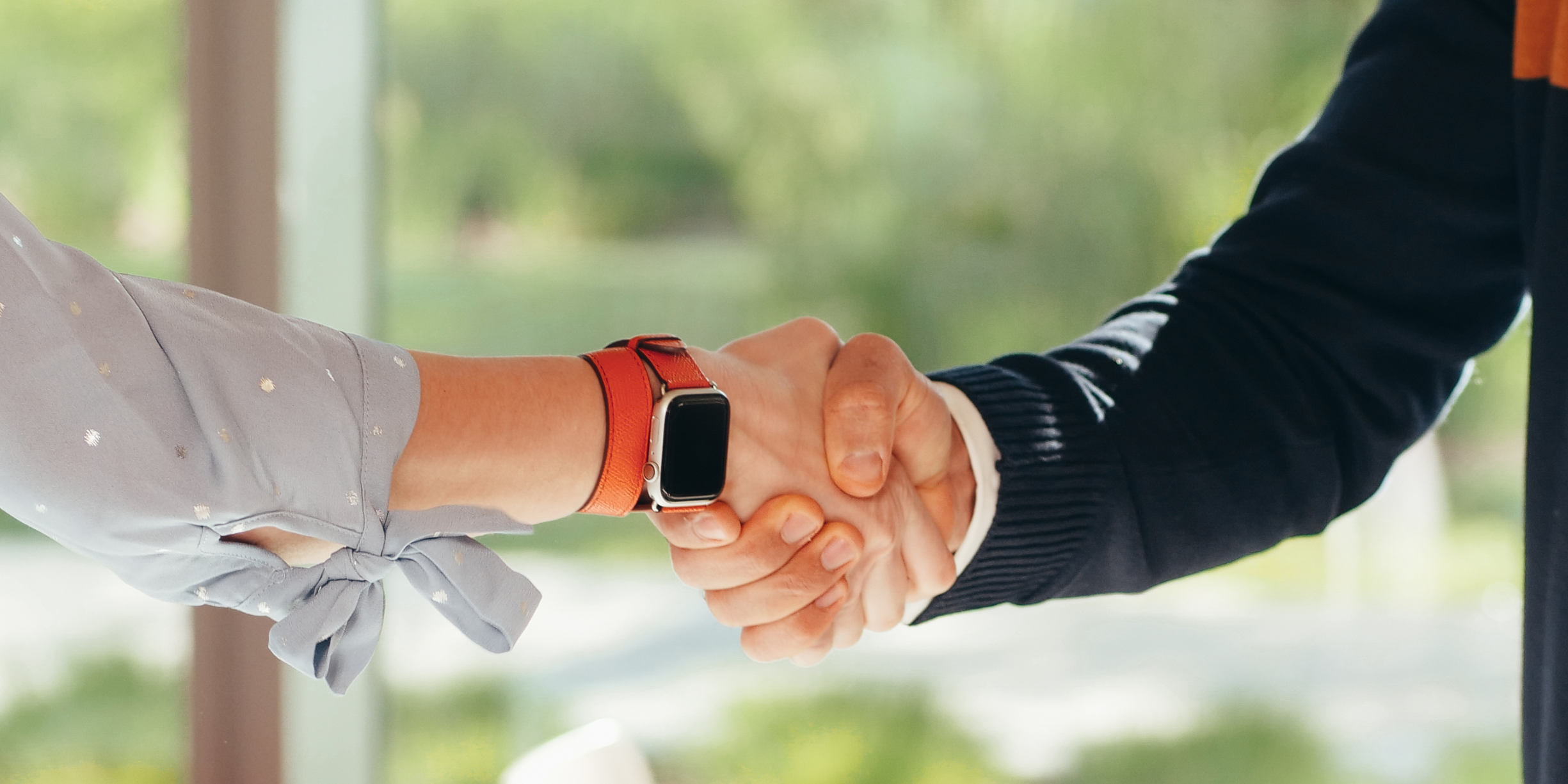 Handshake bras de femme avec montre brune et homme avec chandail de laine bleu marin.