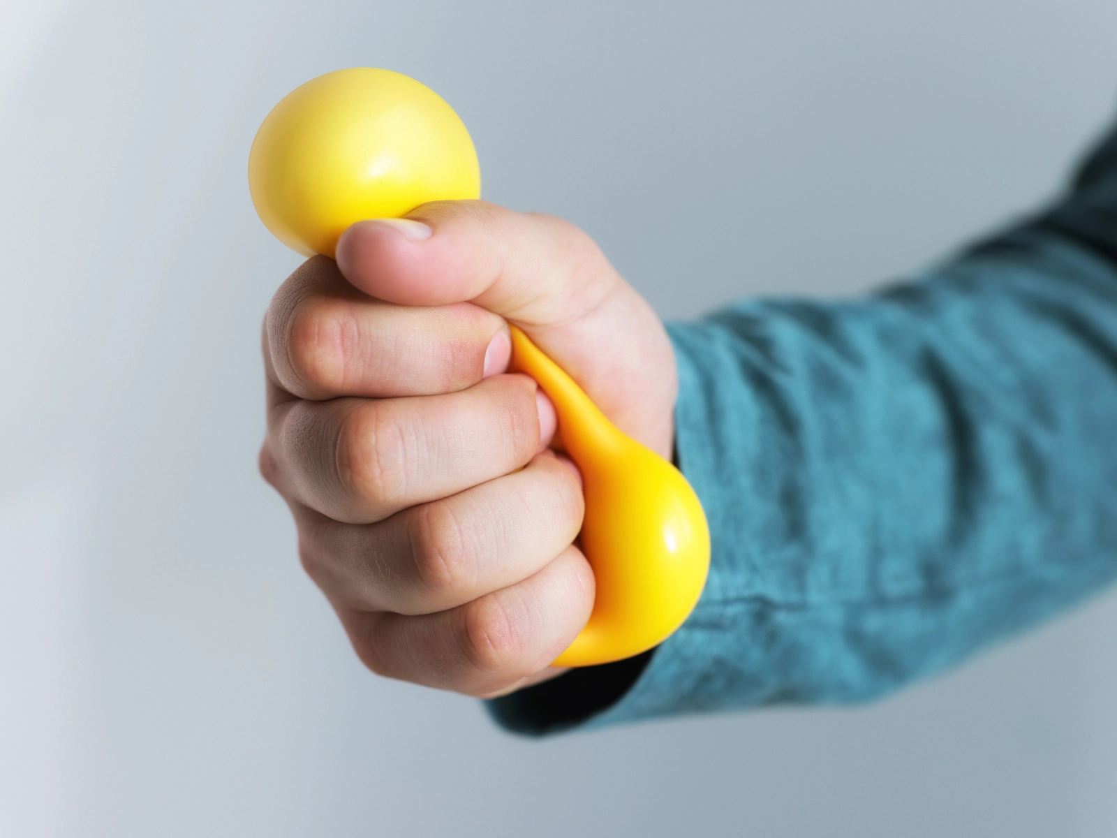 Main qui serre une balle anti-stress jaune.