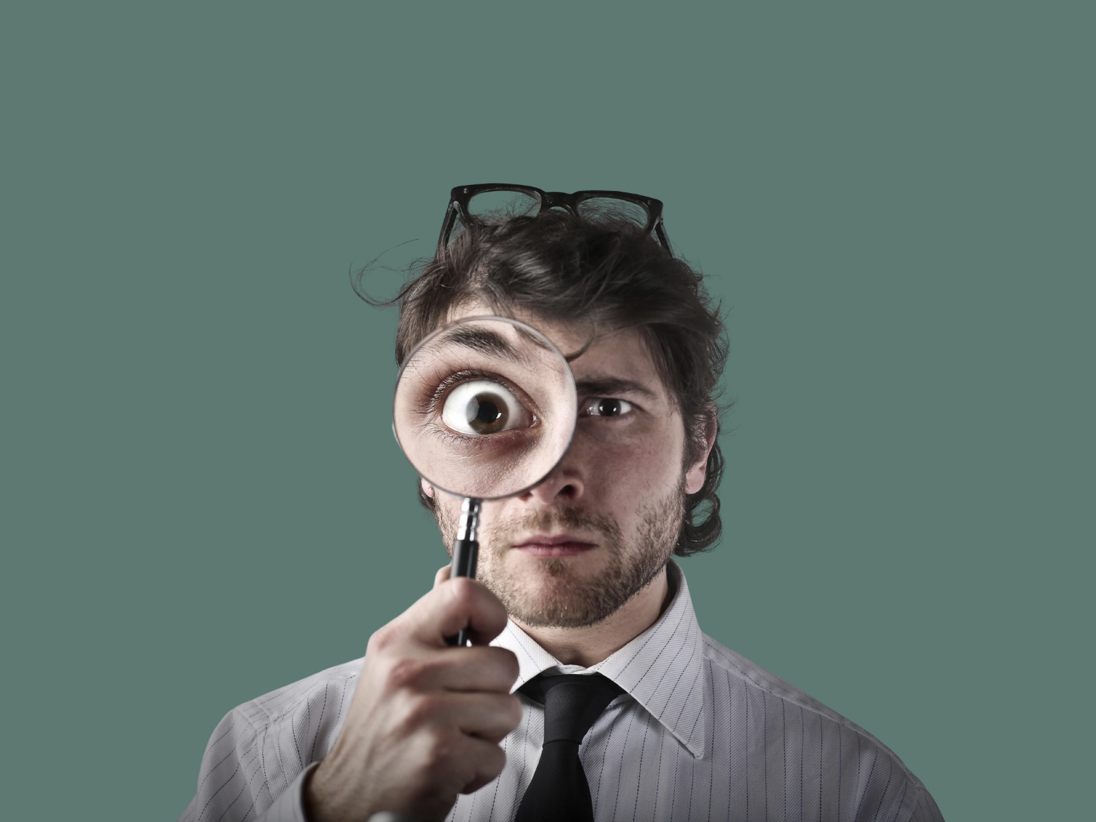 Homme qui regarde dans une loupe. Grand plan sur son oeil. Fond vert.